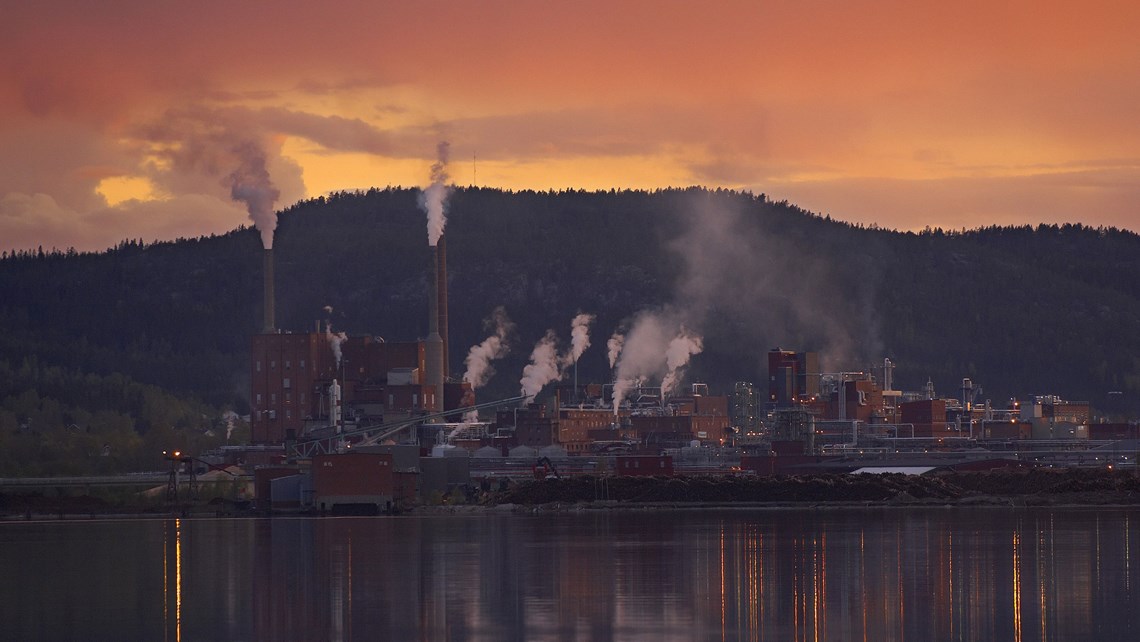 Sonnenuntergang über dem Domsjö-Werk vor einer Waldkulisse und einem Fluss im Vordergrund. Sonnenuntergang über dem Domsjö-Werk vor einer Waldkulisse und einem Fluss im Vordergrund.